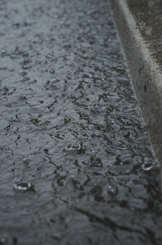 A closeup photo of raindrops splashing in a puddle in the street.