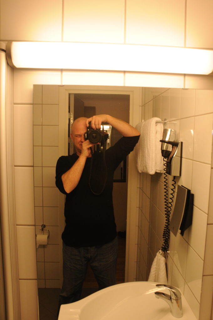 I used a Nikon D300 SLR camera to take a selfie in the mirror in the hotel room in Tromsø. I'm wearing jeans and a long sleeve black t-shirt.