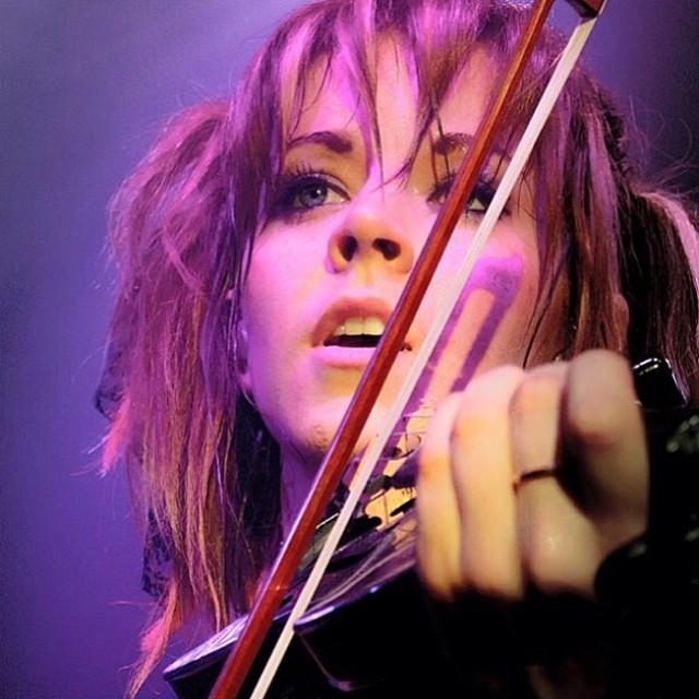 A closeup photo of Lindsey Stirling playing violin on stage.