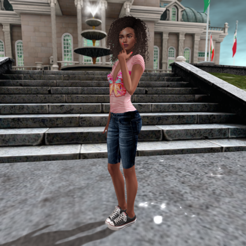 Ayodele Soyinka is posing in front of a royal palace in Second Life. She is wearing a pink t-shirt with a butterfly design on it, denim shorts, and canvas low top sneakers.