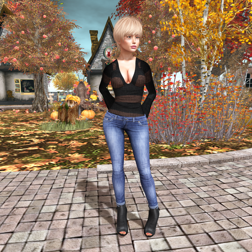 Paola is standing amidst autumn trees and shrubs whose leaves are changing color, She is wearing jeans, boots, and a sweater with a plunging neckline.
